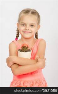 Six year old girl standing with a cactus in a pot, isolated on a light background