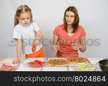 Six year old girl takes a plate of cutting tomatoes for pizza under the supervision of mum
