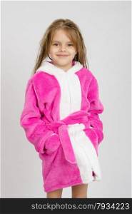Six year old girl with wet hair in a bathrobe on a light background. Portrait of six-year girl in a pink bathrobe