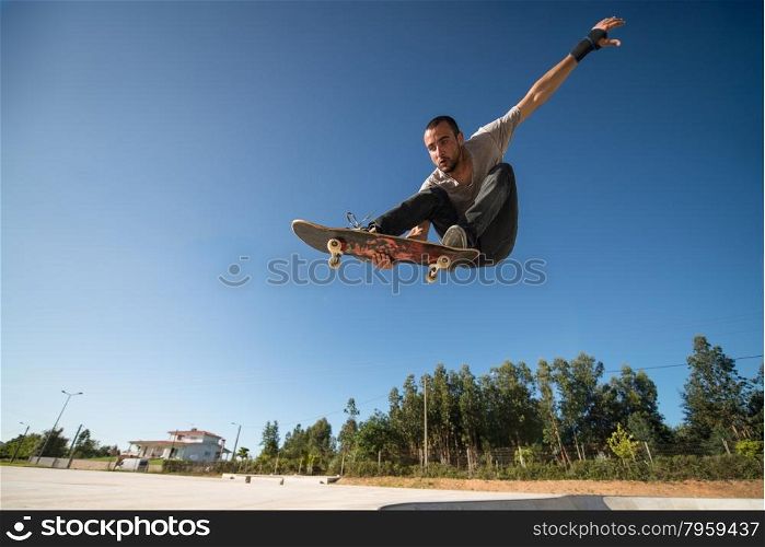 Skateboarder flying over a ramp on blue clear sky.