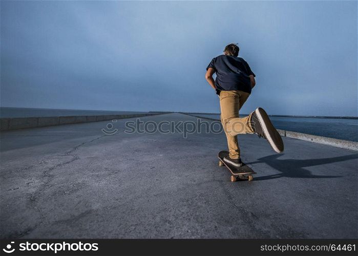 Skateboarder pushing on a concrete pavement along the harbour.