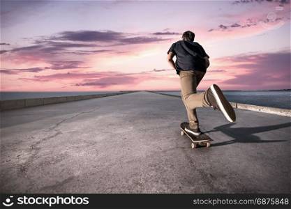 Skateboarder pushing on a concrete pavement along the harbour during the sunset.