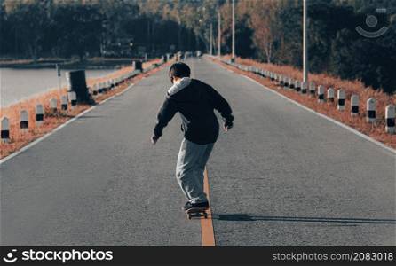 Skateboarder skateboarding on a lakeside road at sunset. Young happy boy skater practicing on skateboard at sunset.