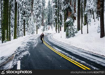 Skateboarder travelling on road in winter landscape, Sequoia National Park, California, USA