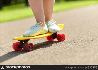 skateboarding, leisure, extreme sport and people concept - close up of teenage girl legs riding short modern cruiser skateboard on road