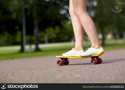 skateboarding, leisure, extreme sport and people concept - close up of teenage girl legs riding short modern cruiser skateboard on road in park