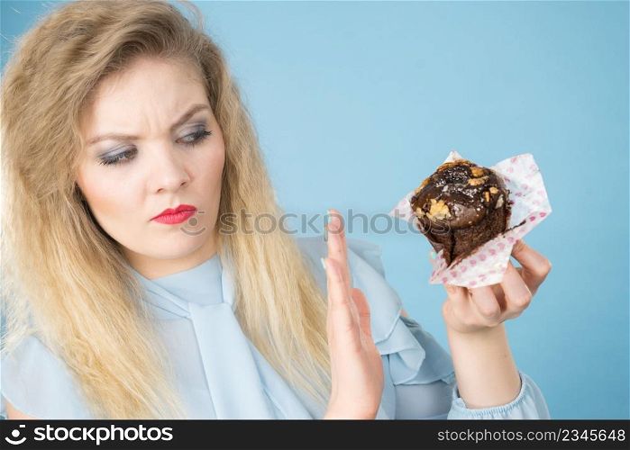 Skeptical woman holding muffin cupcake with dark chocolate flavour having disgusted face expression being on diet. Unhealthy eating, sweet baked food concept.. Skeptical woman holding chocolate cupcake muffin