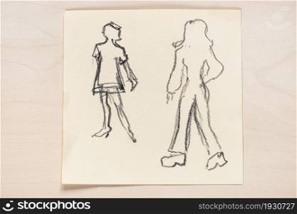 sketch of fashionable silhouette of women of the 60s and the 70s of the XX century hand drawn with black graphite pencil on note paper on light brown table