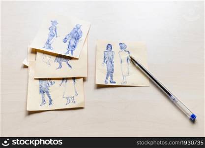 sketches of fashionable silhouette of woman of the XX century hand drawn by blue pen on sheets of paper on light brown table