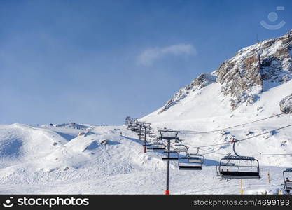 Ski lift in mountains at winter. Alpine winter mountain landscape. French Alps covered with snow in sunny day. Val-d'Isere, Alps, France