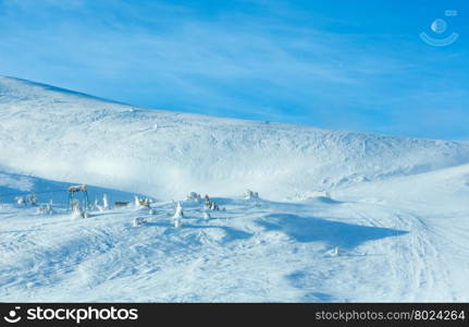 Ski lift on winter morning hill and moon in blue sky.