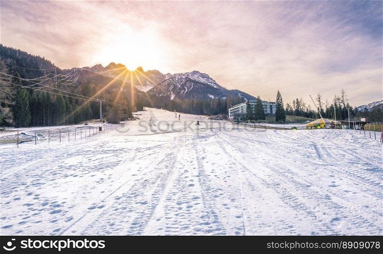 Ski slope on a sunny winter day - Winter landscape with a ski piste, the Austrian Alps mountains and a bright sun. Image taken in Austria.