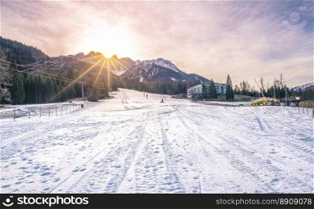 Ski slope on a sunny winter day - Winter landscape with a ski piste, the Austrian Alps mountains and a bright sun. Image taken in Austria.