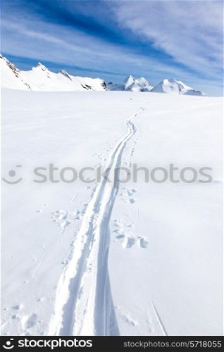 Ski tracks of a backcountry skier on the fresh snow of a large glacier. In background the peaks of Monte Rosa massif - Zermatt, Switzerland, Europe.