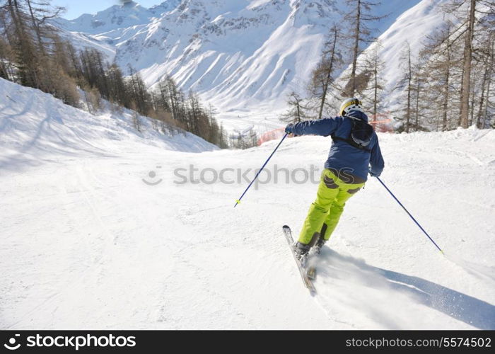 skier skiing downhill on fresh powder snow with sun and mountains in background