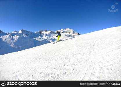 skier skiing downhill on fresh powder snow with sun and mountains in background