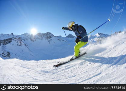 skier skiing downhill on fresh powder snow with sun and mountains in background