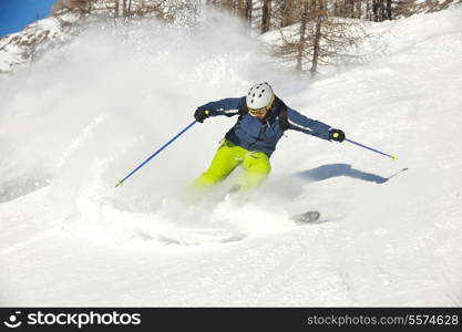 skier skiing downhill on fresh powder snow with sun and mountains in background