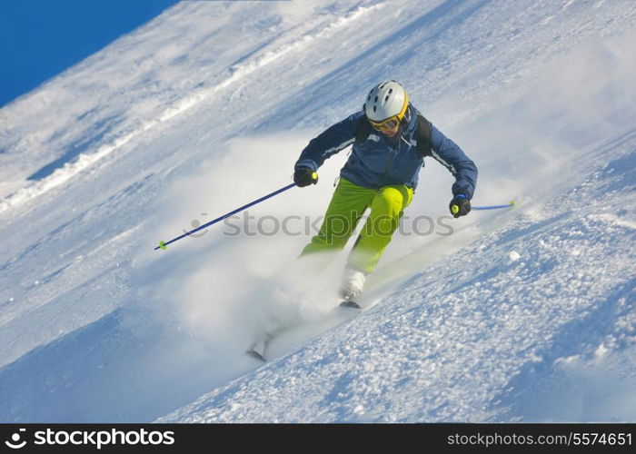 skier skiing downhill on fresh powder snow with sun and mountains in background