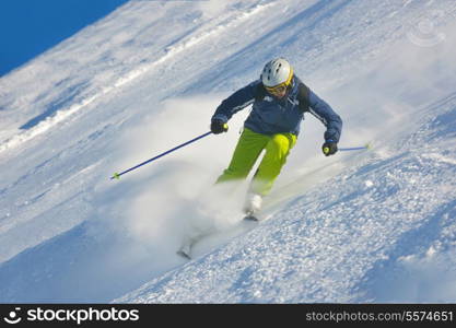 skier skiing downhill on fresh powder snow with sun and mountains in background