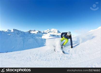 skier skiing downhill on fresh powder snow with sun and mountains in background