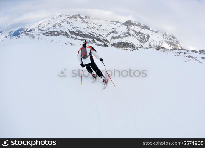 skier skiing downhill on fresh powder snow with sun and mountains in background