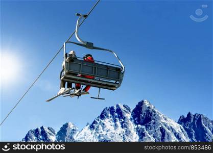 Skiers on a ski lift in high mountains on the background of a clear blue sky with copy space.