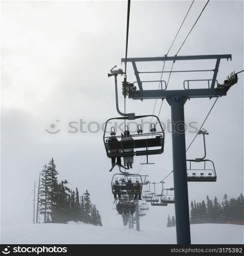 Skiers riding the chairlift in foggy winter weather.