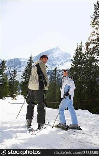 Skiing couple looking over shoulder standing on ski slope back view