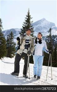 Skiing couple standing carrying skis on shoulders on ski slope