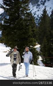 Skiing couple walking carrying skis on shoulders on ski slope