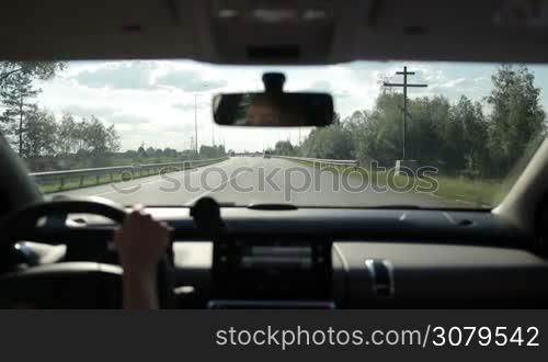 Skilful female driver driving car on highway during summer road trip. View from inside of auto. Woman driving vehicle on freeway in sunlight with traffic on background.