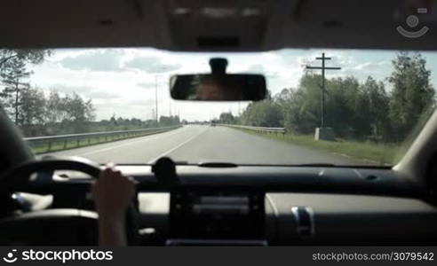 Skilful female driver driving car on highway during summer road trip. View from inside of auto. Woman driving vehicle on freeway in sunlight with traffic on background.