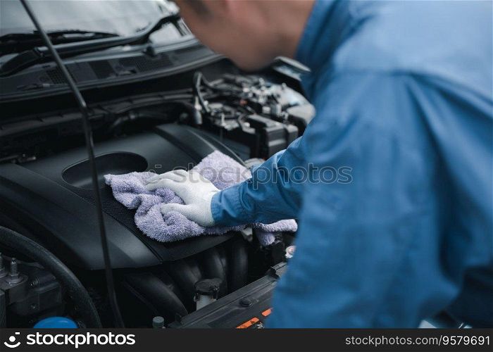 Skilled Asian mechanic in blue shirt writing notes on a paper, while working on a car in an auto repair shop. Close-up shot of hand.
