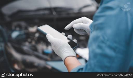 Skilled repairman using smartphone to diagnose car issues at garage. Close up of mechanic’s hand holding wrench while examining engine. Horizontal photography with workshop background.