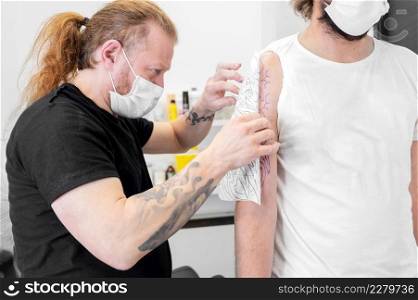 Skilled Tattoo artist putting a sketch on the arm of a man. High quality photo. Skilled Tattoo artist putting a sketch on the arm of a man.