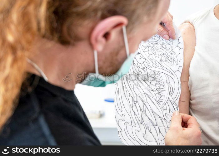 Skilled Tattoo artist putting a sketch on the arm of a man. High quality photo. Skilled Tattoo artist putting a sketch on the arm of a man.