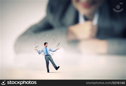 Skillful businessman. Businesswoman looking at miniature of man juggling with items