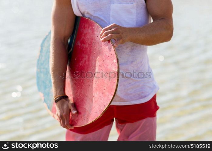 skimboarding, water sport and people concept - close up of young man with skimboard on summer beach. close up of man with skimboard on summer beach