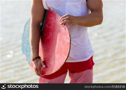skimboarding, water sport and people concept - close up of young man with skimboard on summer beach. close up of man with skimboard on summer beach