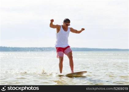 skimboarding, water sport and people concept - happy young man riding on skimboard on summer beach. young man riding on skimboard on summer beach
