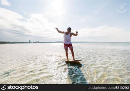 skimboarding, water sport and people concept - happy young man riding on skimboard on summer beach. young man riding on skimboard on summer beach