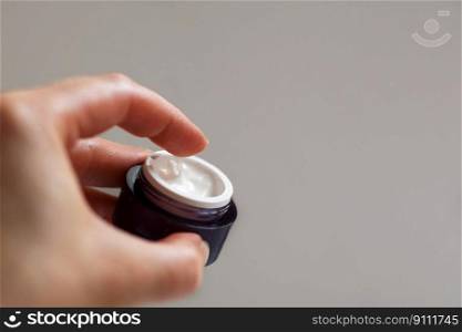 Skin and body care. Hands of a girl with a jar of face cream close up applied to the finger of woman&rsquo;s hand on light background. Hands of a girl with a jar of face cream close up applied to the finger of woman&rsquo;s hand on light background