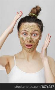 Skin Care. Cosmetic Day. Amazed young girl in home style, her hair gathered with her hands at the top. With eco, herbal, natural mask, green on the face. Front view.. Skin Care. Cosmetic Day. Amazed young girl in home style