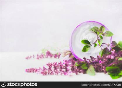 Skin care cream in jar with purple herbs on white wooden background. Natural cosmetic concept