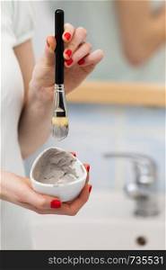 Skin care. Female hand holding brush and clay mud mask to apply on skin face, in bathroom. Girl taking care of her oily compexion. Spa wellbeing.. Female hand holding clay mud mask and brush. Skin care.