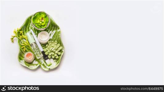 Skin care setting . Herbal cosmetic concept. Tropical leaves and succulents with cosmetic products and accessories: Mask Brush, bowl and flowers on white desktop background, top view, copy space