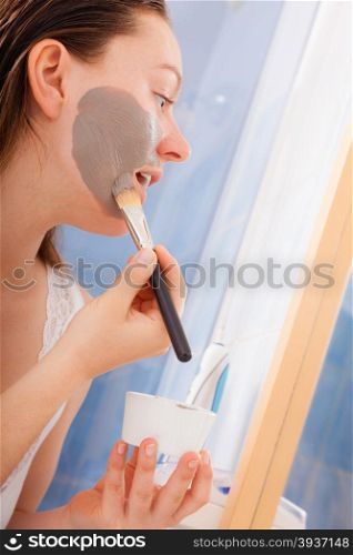 Skin care. Young woman applying with brush mud mask on face in bathroom