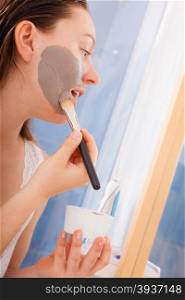Skin care. Young woman applying with brush mud mask on face in bathroom