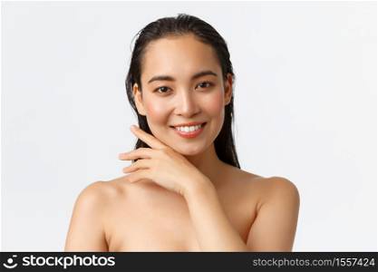 Skincare, bodycare, beauty and bath concept. Close-up of sensual attractive asian woman standing naked in shower, smiling and gently touching face, promo of facial products, white background.. Skincare, bodycare, beauty and bath concept. Close-up of sensual attractive asian woman standing naked in shower, smiling and gently touching face, promo of facial products, white background